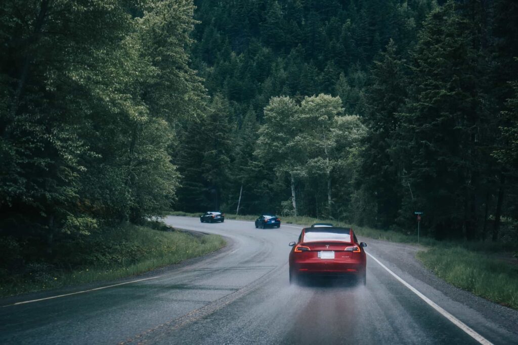 Tesla-biler på landevei omringet av skog
